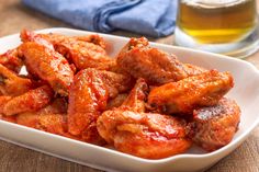 chicken wings are in a white dish next to a glass of beer