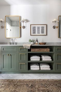 a bathroom with green cabinets and white towels on the counter top, gold framed mirrors above it