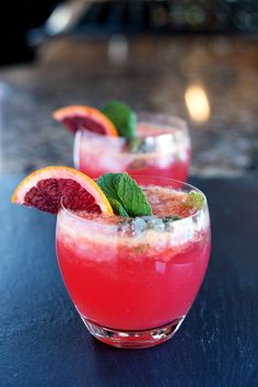 two glasses filled with fruit and ice on top of a blue countertop next to each other