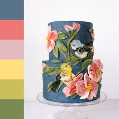 a three tiered cake decorated with flowers and birds on blue icing, sitting on a clear plate