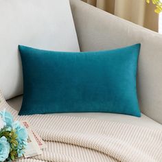 a blue pillow sitting on top of a white couch next to a vase with flowers