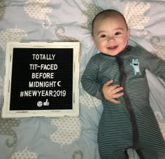 a baby laying on top of a bed next to a sign