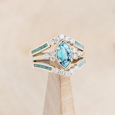 a blue and white stone ring sitting on top of a wooden stand with diamond accents