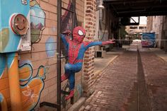 a spiderman statue is hanging on the side of a building in front of a brick wall