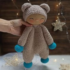 a hand holding a small stuffed animal in front of a christmas tree with lights behind it