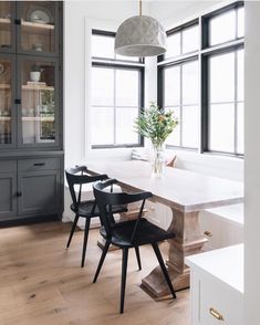 a dining room table with two chairs and a vase on top of it in front of windows