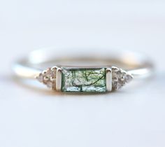 Moss agate engagement ring with a baguette-cut green mossy agate and accent moissanites or white diamonds. The prices listed are for the moss agate ring only. Please see the set with the lace band here: https://www.etsy.com/listing/883584053 We are the original jewelry designers to use moss agate and create geometric moss agate one of a kind jewelry. Please beware of other jewelry designers using moss agate as their designs are replicas of our bestsellers and cannot match our high standards of p Engagement Ring Baguette, Green Agate Ring, Baguette Engagement Ring, Ring Baguette, Moss Agate Engagement Ring, Alternative Wedding Rings, Gemstone Wedding Rings, Green Gemstone Ring, Agate Engagement Ring