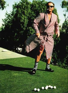 a man in a robe is playing golf on the green with white balls behind him