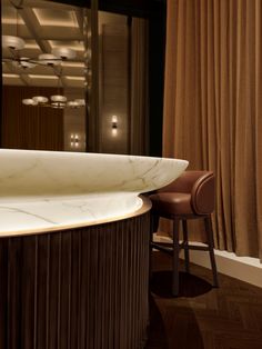 a marble counter top sitting next to a brown chair in front of a curtained window