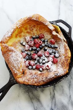 an iron skillet with berries and powdered sugar in it on a marble surface