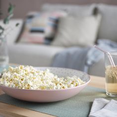 a bowl of popcorn and a glass of water on a table with a couch in the background