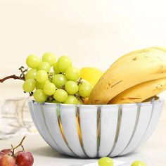 a bowl filled with grapes and bananas on top of a table next to other fruits