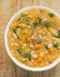 a white bowl filled with soup sitting on top of a wooden table next to a spoon