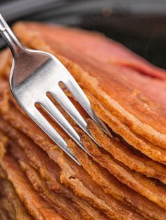 a close up of a fork on top of some bacon pancakes with other meats in the background