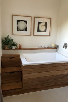 a bathroom with two framed pictures above the bathtub and drawers on the wall next to it