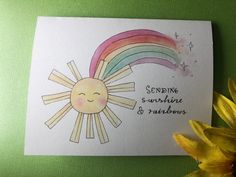 a card with a sun and rainbow painted on it next to a yellow flower that says sending sunshine & rainbows