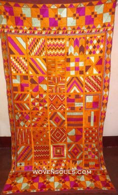 an orange and pink quilt hanging on a wall