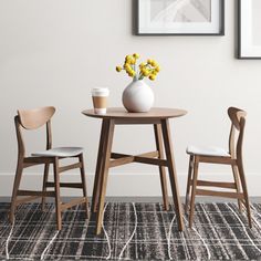 a table with two chairs and a vase filled with flowers on top of it next to a wall