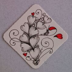 a white square coaster with hearts and birds on the top, sitting on a gray surface