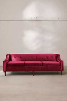 a red couch sitting on top of a white floor next to a wall and window