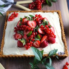 a cake with strawberries and berries on top is sitting on a table next to some leaves