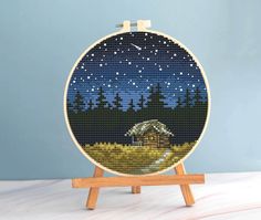 a cross stitch picture of a cabin in the woods at night with stars and moon