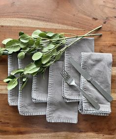 four napkins with silverware and green leaves on them sitting on a wooden table