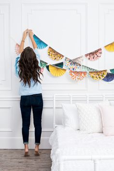 a woman standing in front of a bed with paper fans hanging on the wall above her head