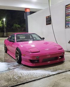 a pink car is parked in front of a gas station with water coming out of it