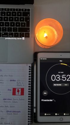 an open laptop computer sitting on top of a desk next to a smart phone and a lit candle