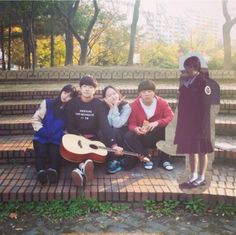 a group of young people sitting on the steps in front of some stairs with an acoustic guitar