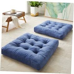 two blue futons sitting on the floor in front of a painting and coffee table