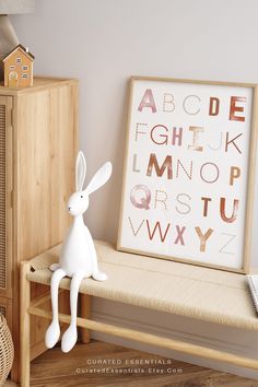 a white rabbit sitting on top of a wooden bench next to a framed letter print