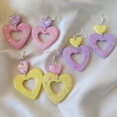 four heart shaped earrings sitting on top of a white cloth covered bedding with pink, yellow and blue hearts hanging from them