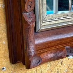 an ornate wooden frame on the side of a wall with a mirror above it and a cat sitting in the window