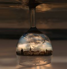 an upside down view of a city in a wine glass that is reflecting the sky and clouds