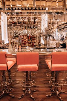 three orange chairs sitting at a bar with wine glasses on it