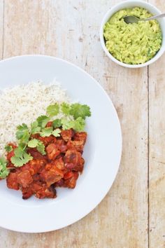 a white plate topped with rice and meat next to a bowl of guacamole