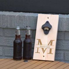 two bottle openers sitting on top of a wooden sign next to two beer bottles