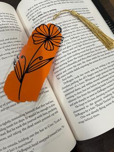 an orange bookmark with a flower on it sitting in front of an open book