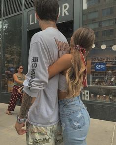 a man and woman standing in front of a store with their arms around each other