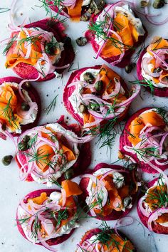 an assortment of food is displayed on a white table top, including red onions and carrots