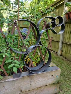 a metal sculpture sitting on top of a wooden box filled with flowers and plants next to a fence