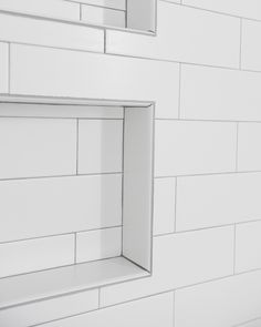 a white tiled bathroom with two mirrors above the sink and one shelf on the wall