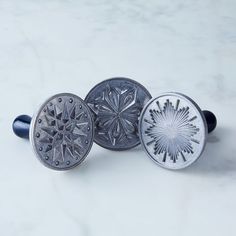 three metal buttons with designs on them sitting on a marble counter top next to each other