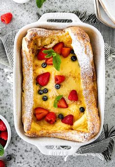 a cake with berries and powdered sugar in a white dish on a gray table