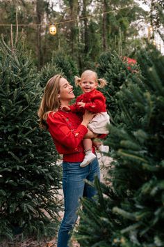 a woman holding a toddler in her arms while standing between rows of christmas trees