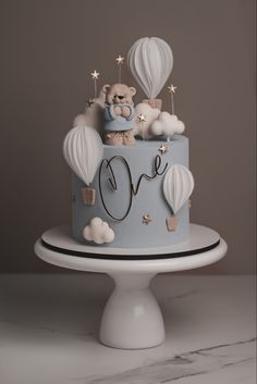 a blue and white cake with teddy bears on top is sitting on a pedestal in front of a gray background