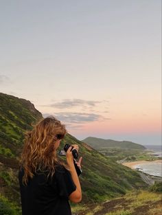 a woman standing on top of a lush green hillside with a camera in her hand