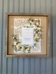 a framed paper doily with flowers on it and a wedding card in the middle